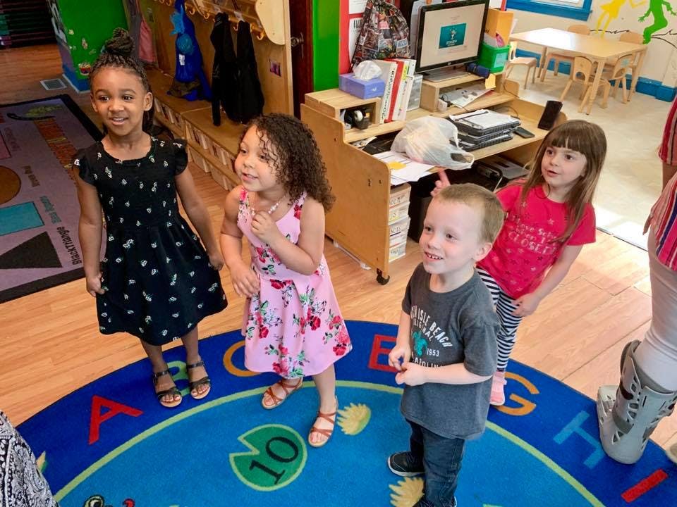 Four children standing on a rug in a classroom