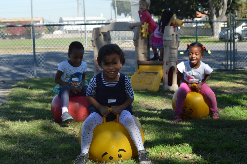 Three children playing on bouncy toys in a grassy area