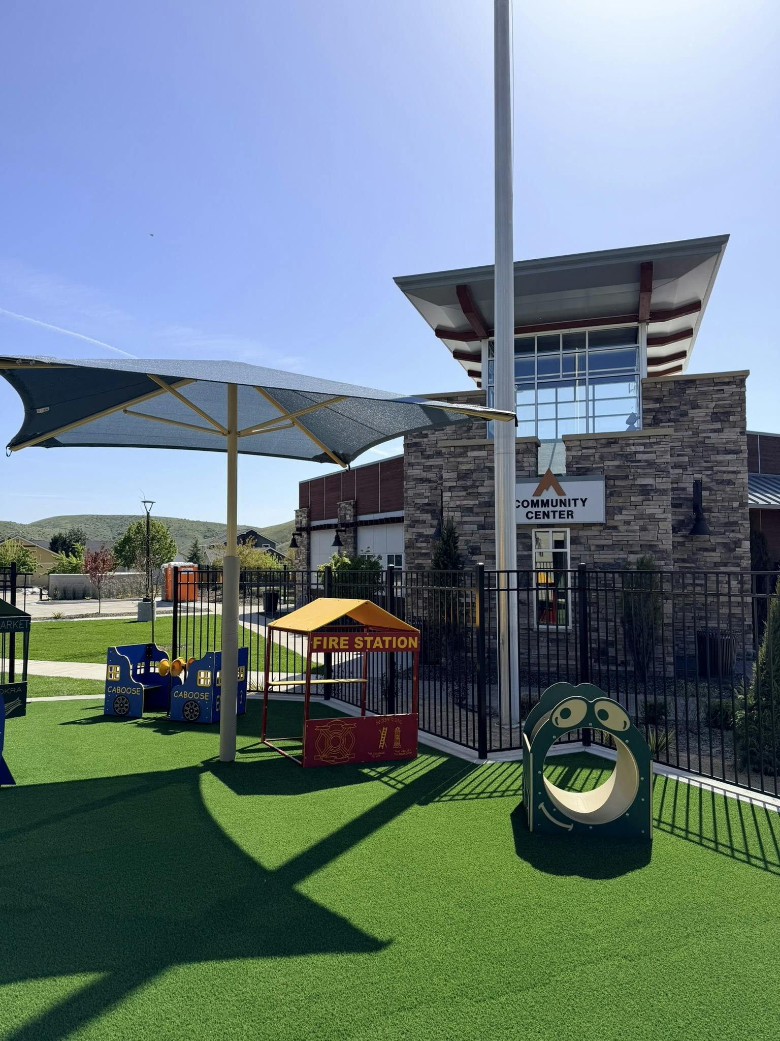 Playground with shade structure, play fire station, and community center in background