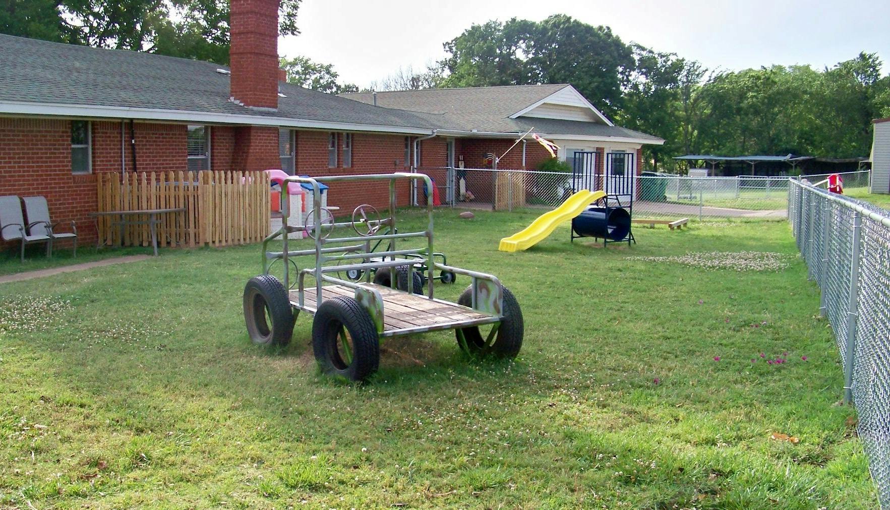 Homemade go-kart in a grassy yard with a building and slide in the background