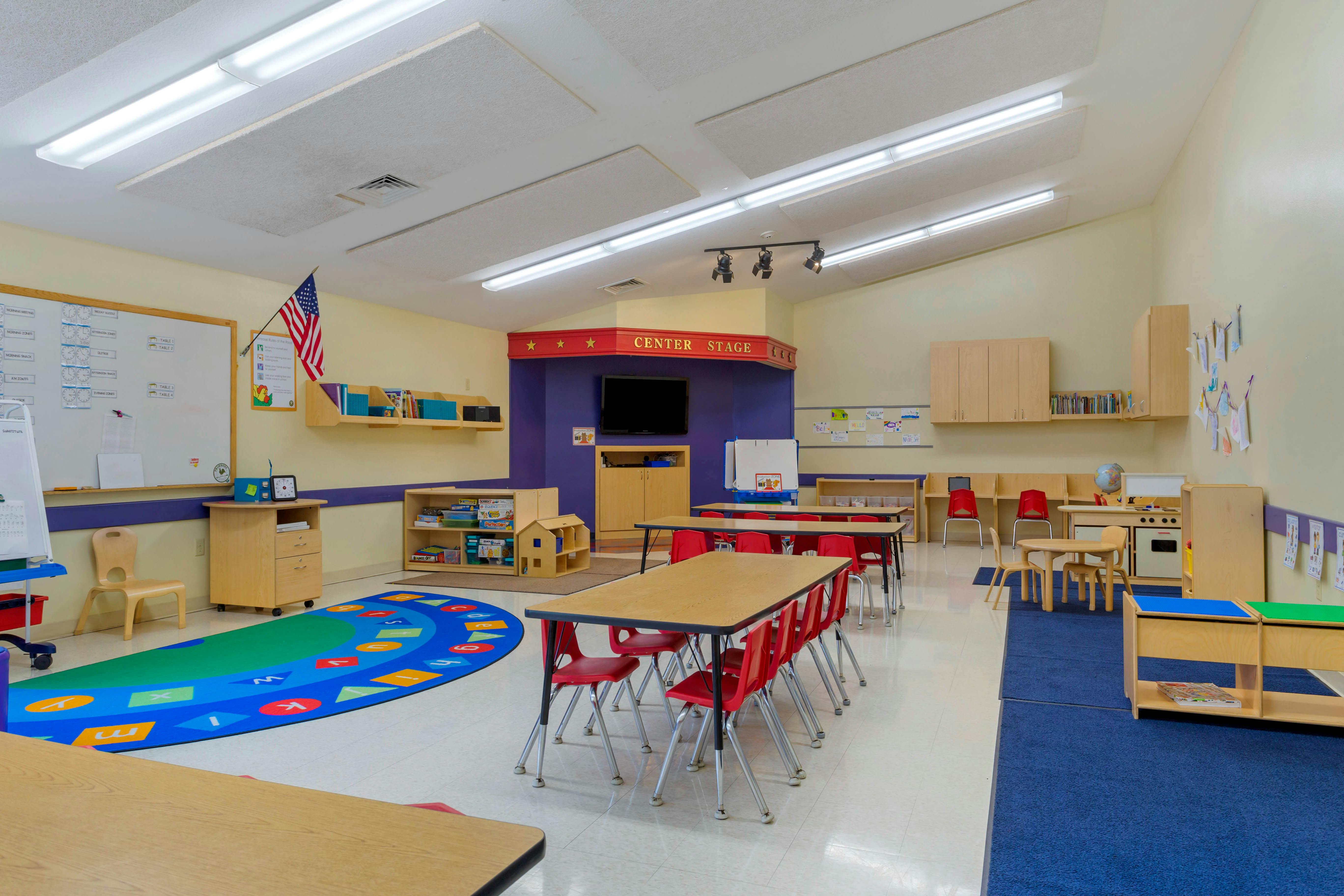 Classroom with tables, red chairs, and a play area with area a large rug