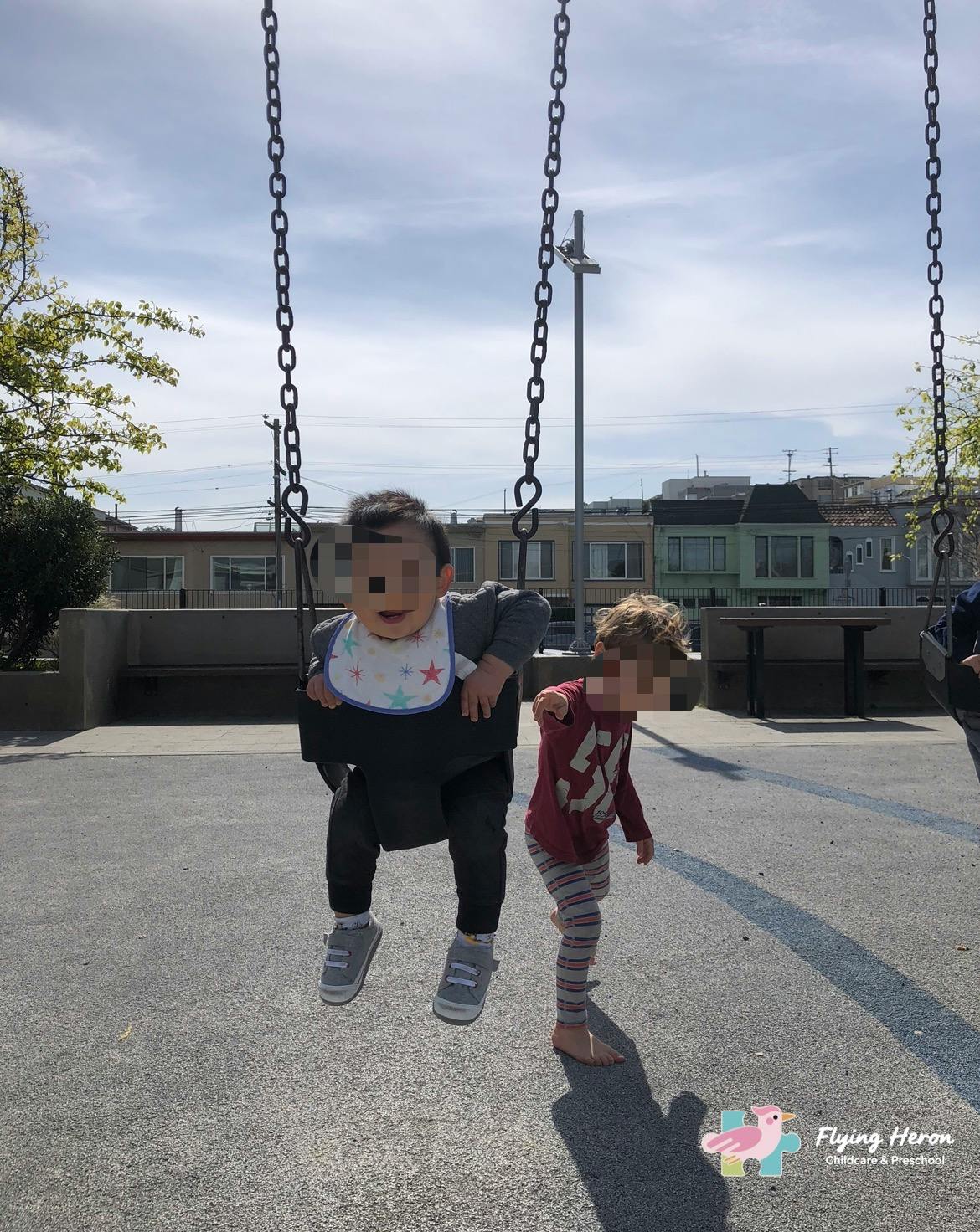Child in a swing with another child standing nearby on a playground