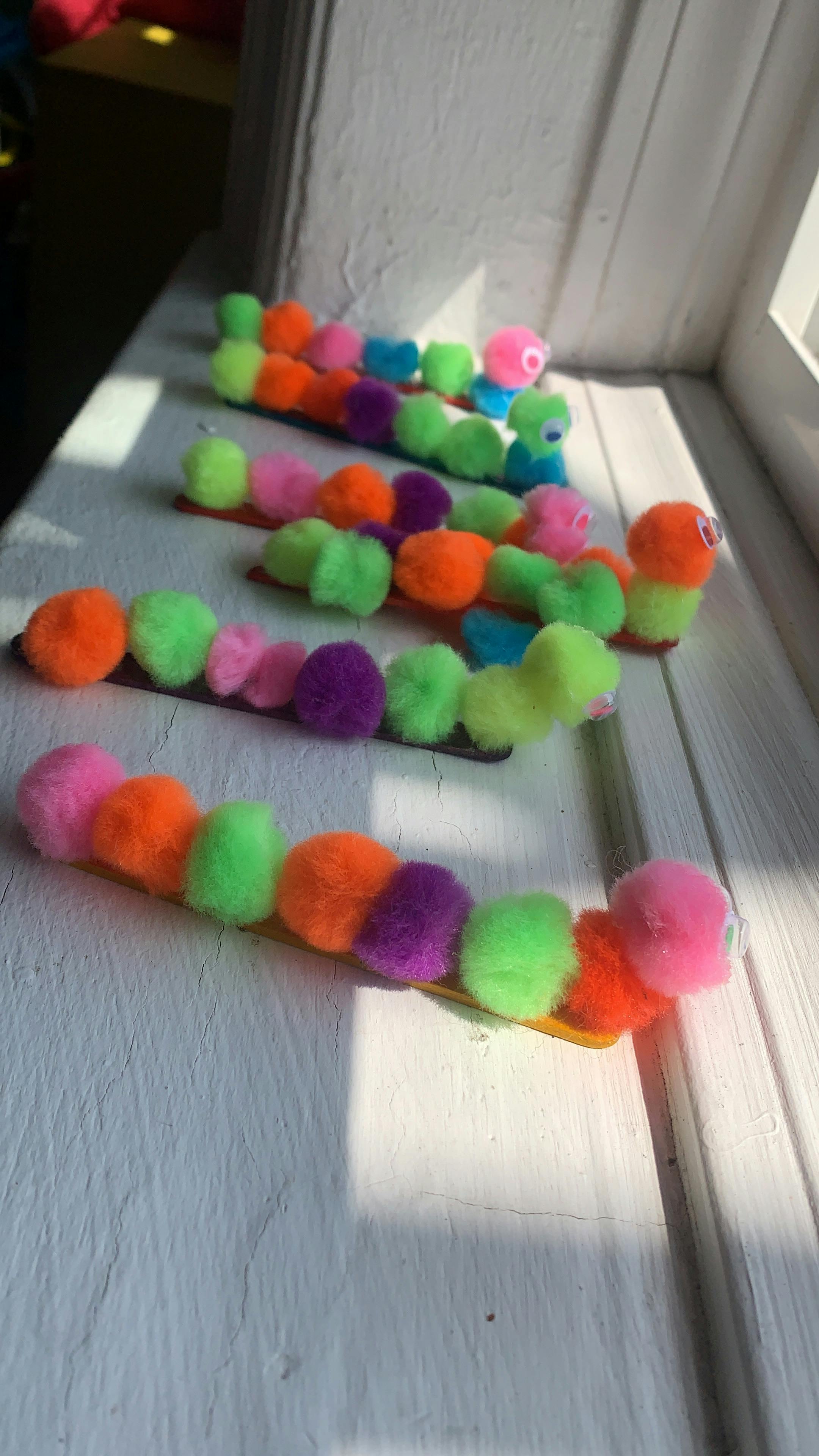 Multiple colorful pom-pom caterpillars on a white surface