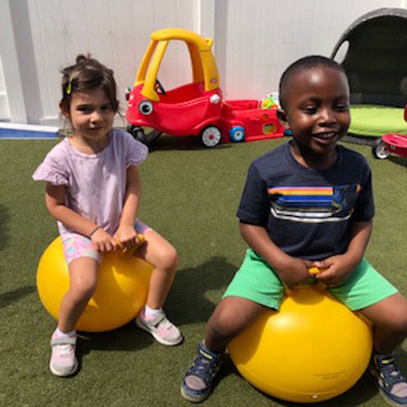 Two children sitting on yellow hopper balls outdoors