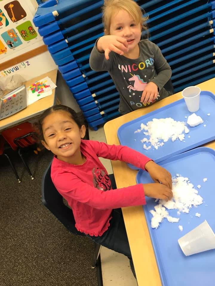 Two children playing with white material on blue trays at a table