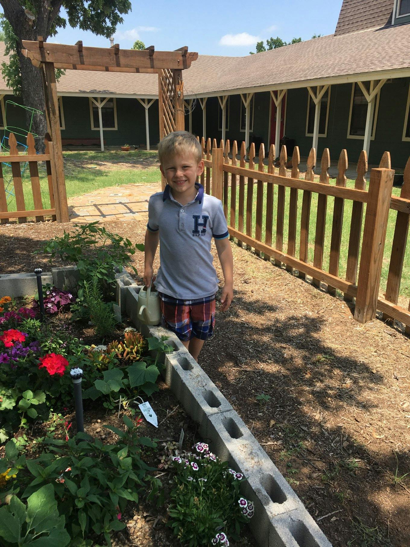 Child standing in a garden next to a flower bed