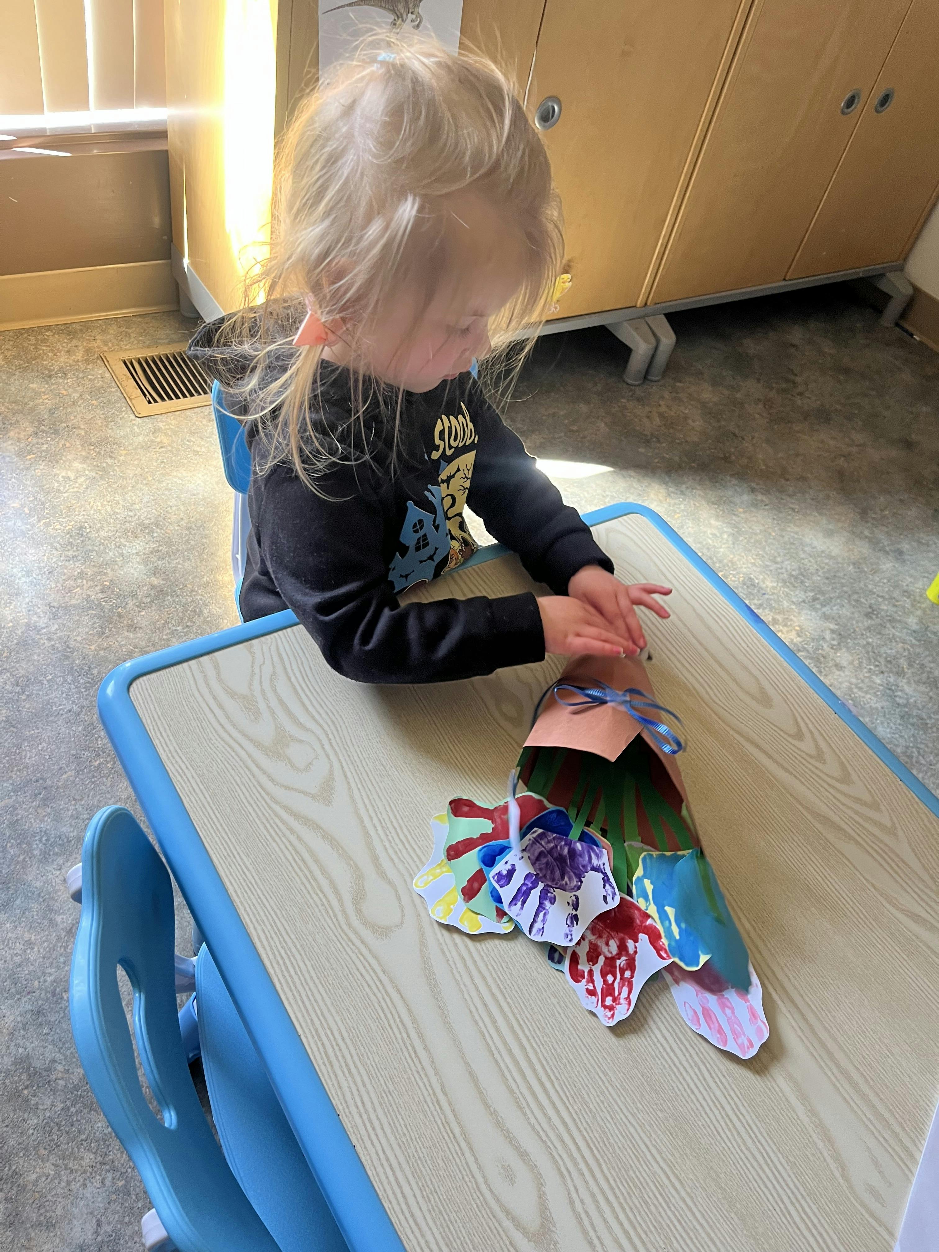 Child at a table touching a paper craft made with handprints