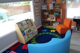 Children's reading nook with a bookshelf, two chairs, and a colorful rug
