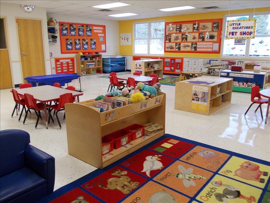 Classroom with small tables and chairs, shelves, and a colorful rug