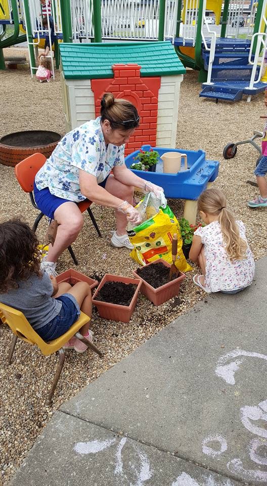 Person pouring soil from a bag into pots with two children nearby