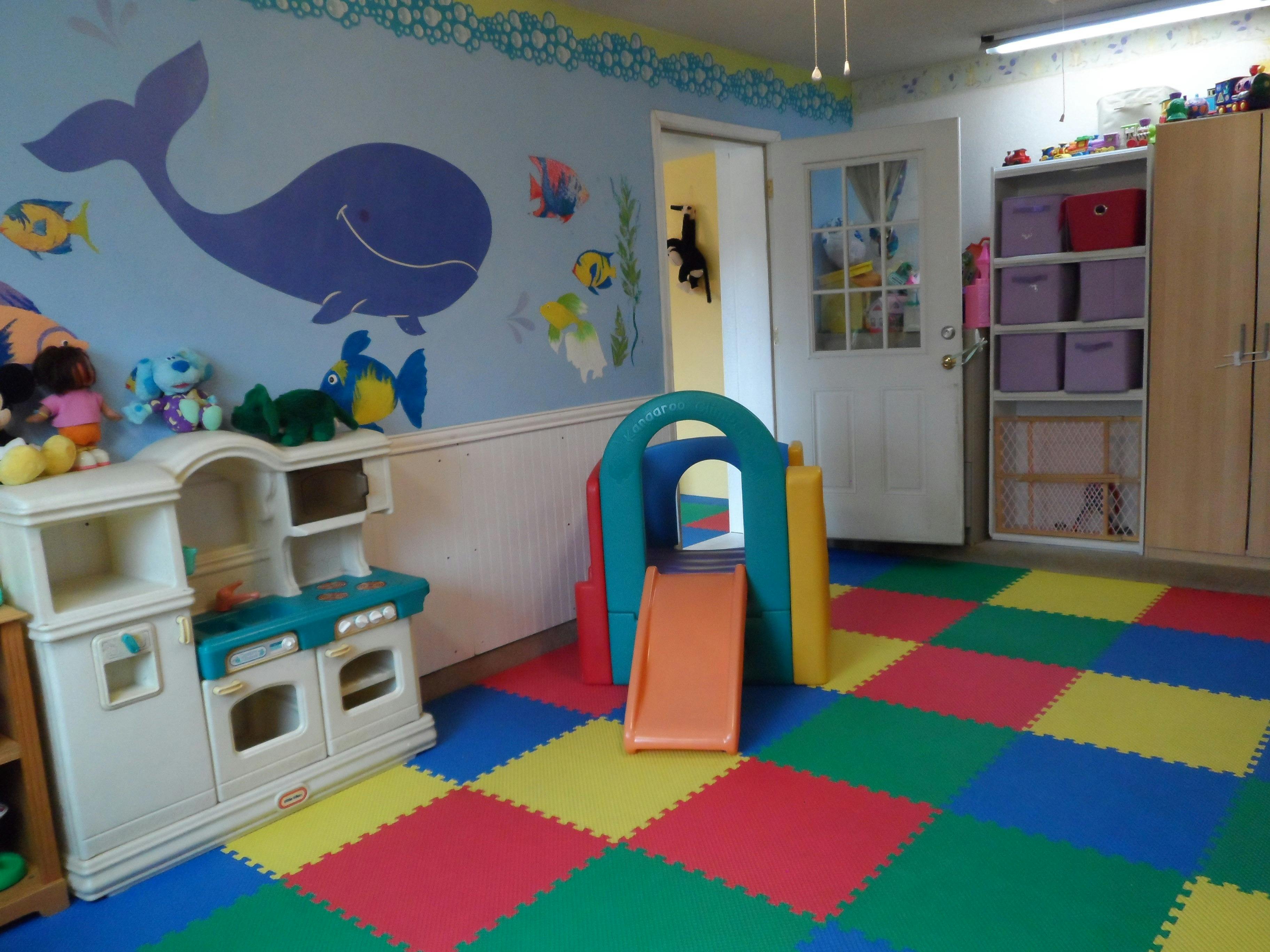 Playroom with colorful floor mats, toy kitchen, and small slide
