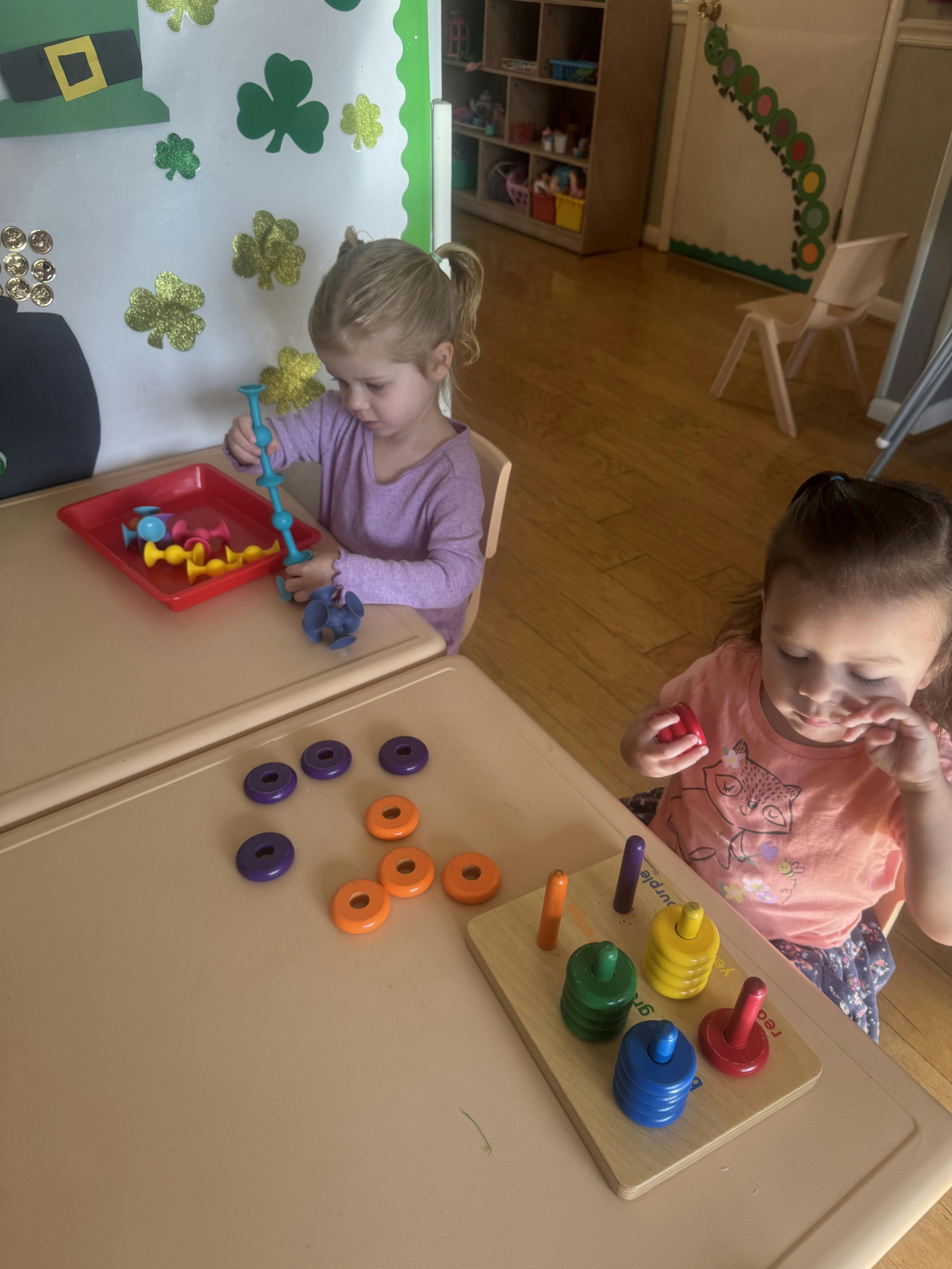 Two young children playing with sorting toys at small tables in a classroom