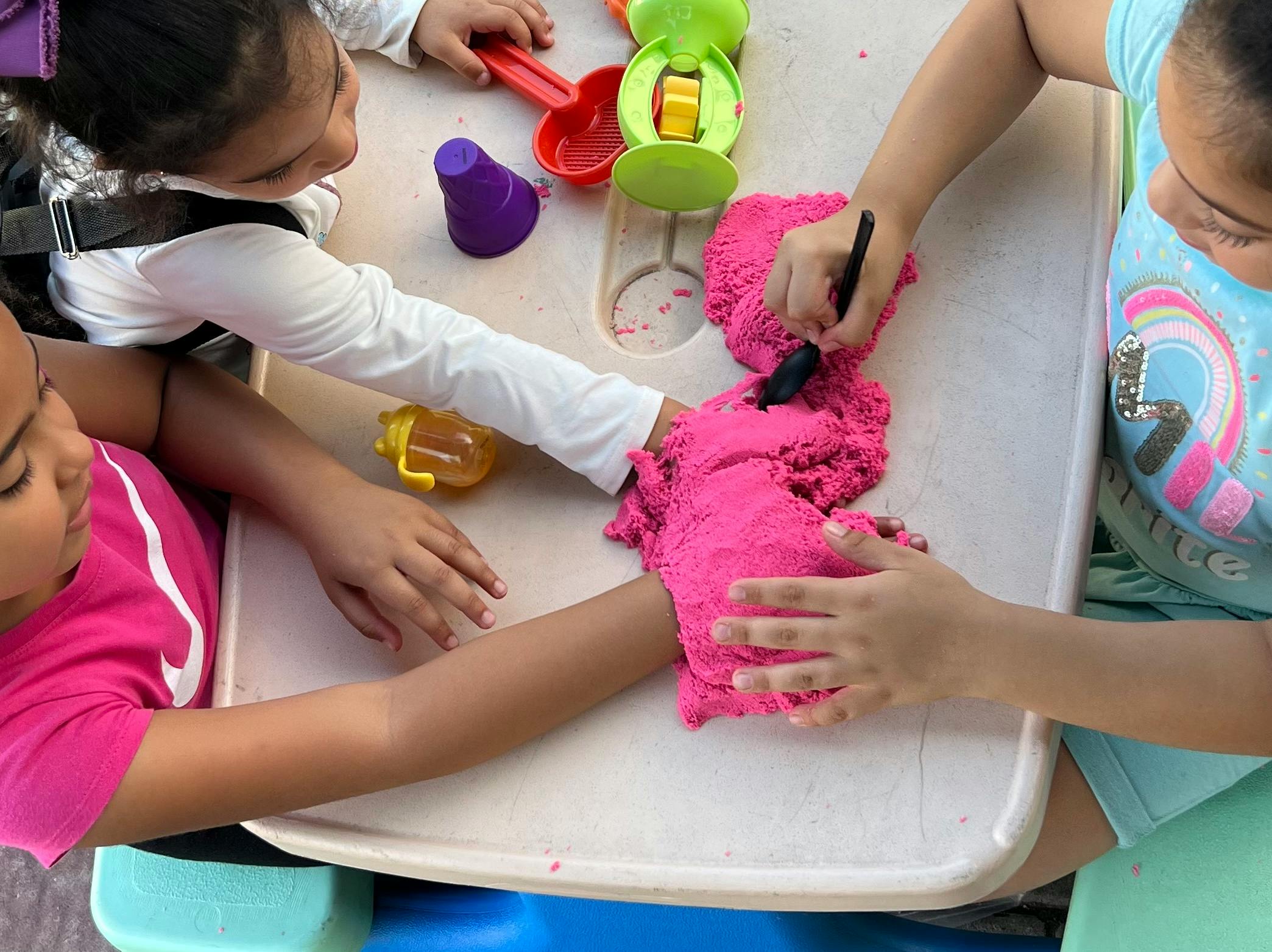 Children playing with pink kinetic sand at a table