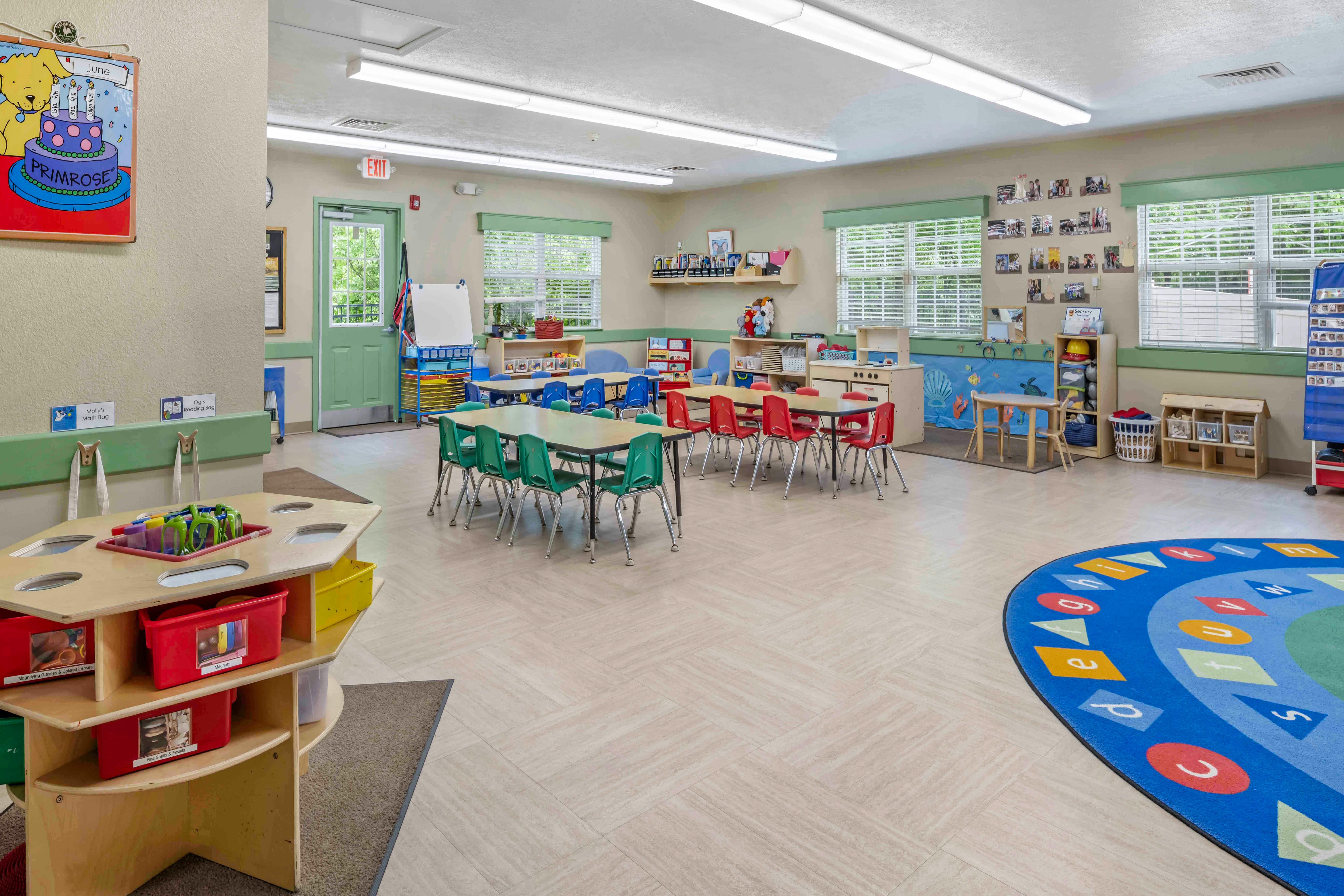 Classroom with small tables and chairs, a blue circular rug with letters and shapes