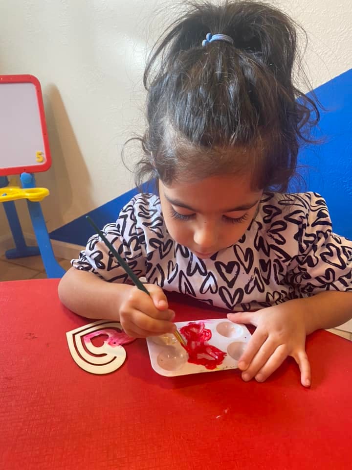 Child painting a heart shape with red paint