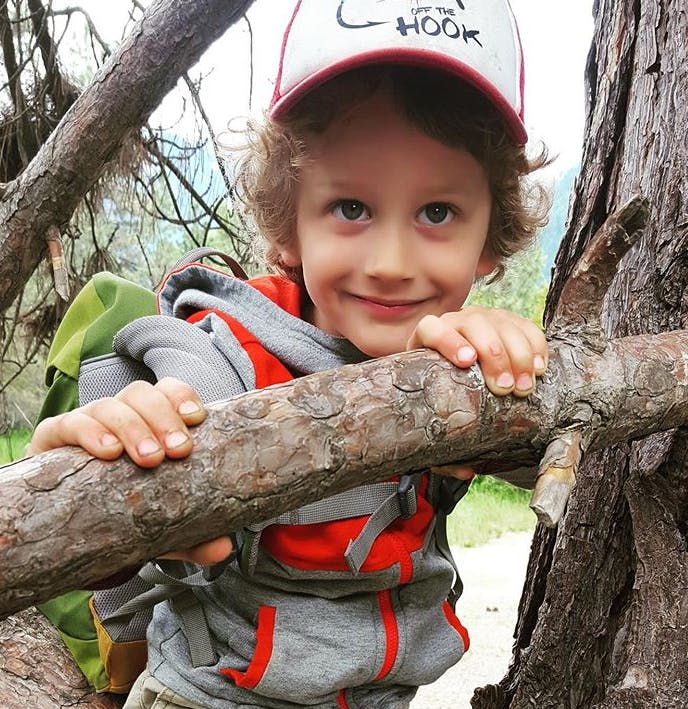 Child in a hat holding onto a tree branch