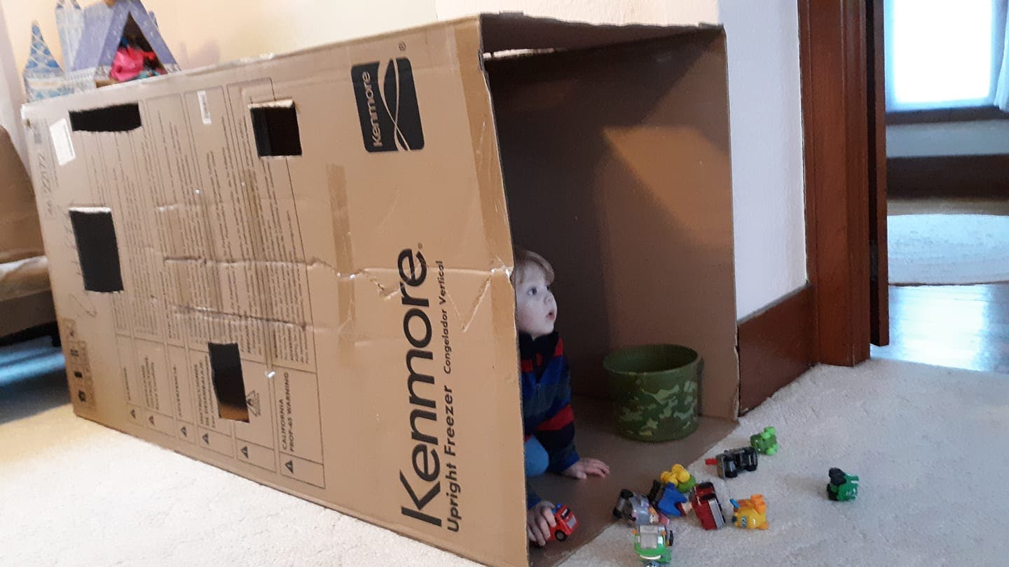 Child playing inside a large cardboard box with toys