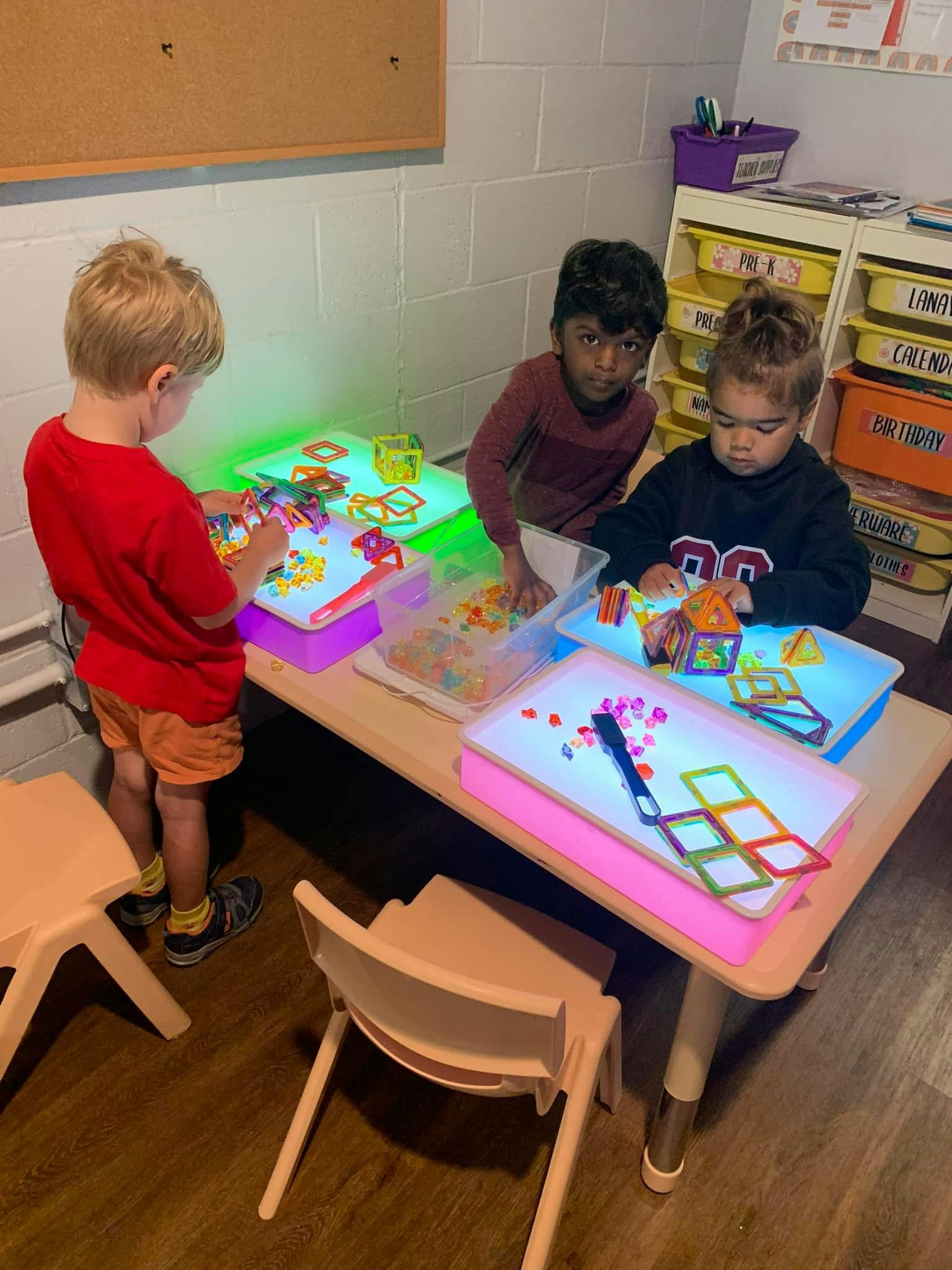 Three children playing with light tables and colorful magnetic shapes