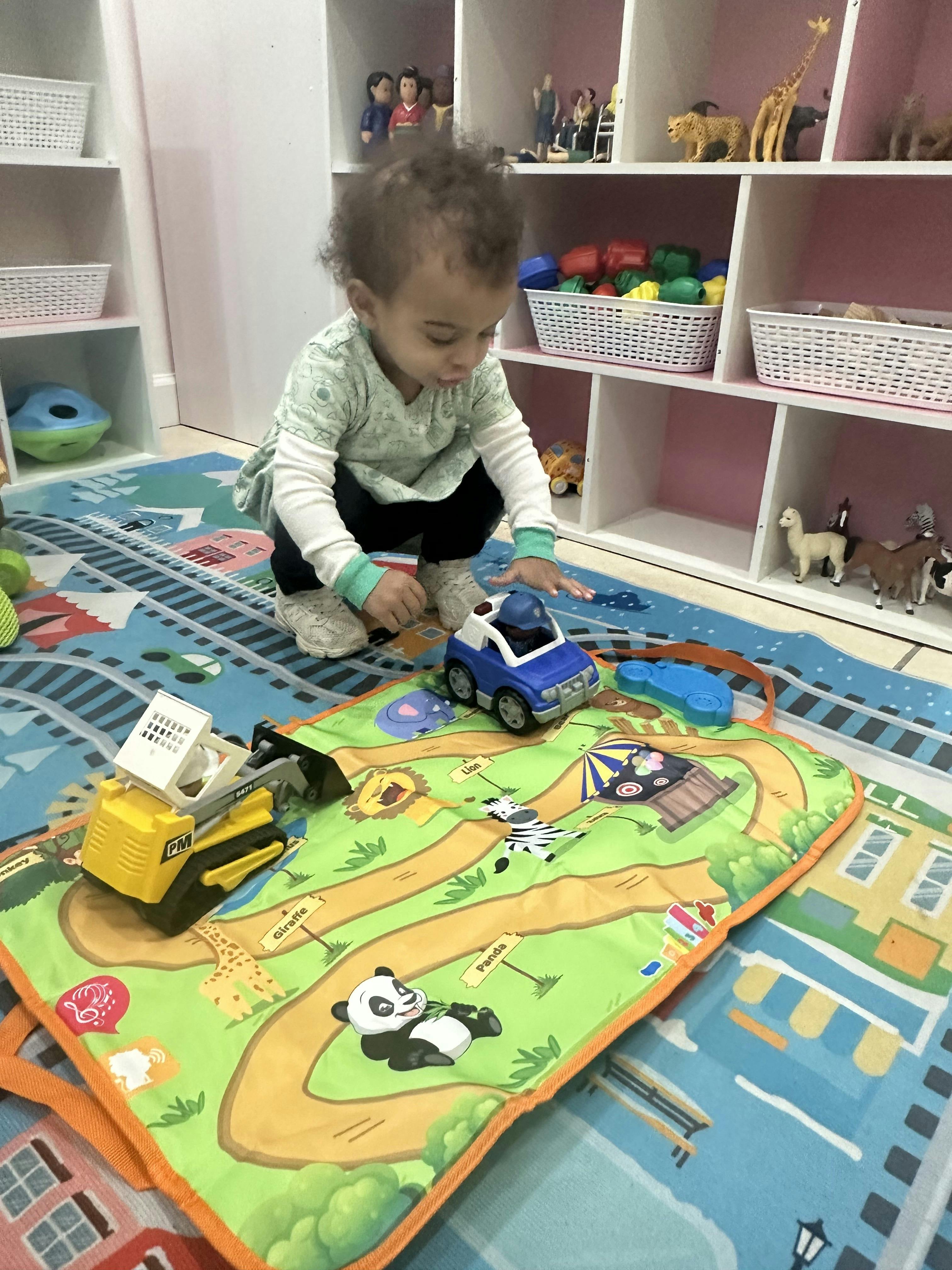 Child crouching on a playmat, reaching for a toy police car