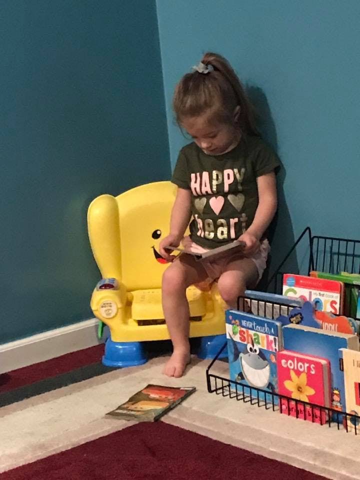 Child sitting in a yellow chair and reading a book