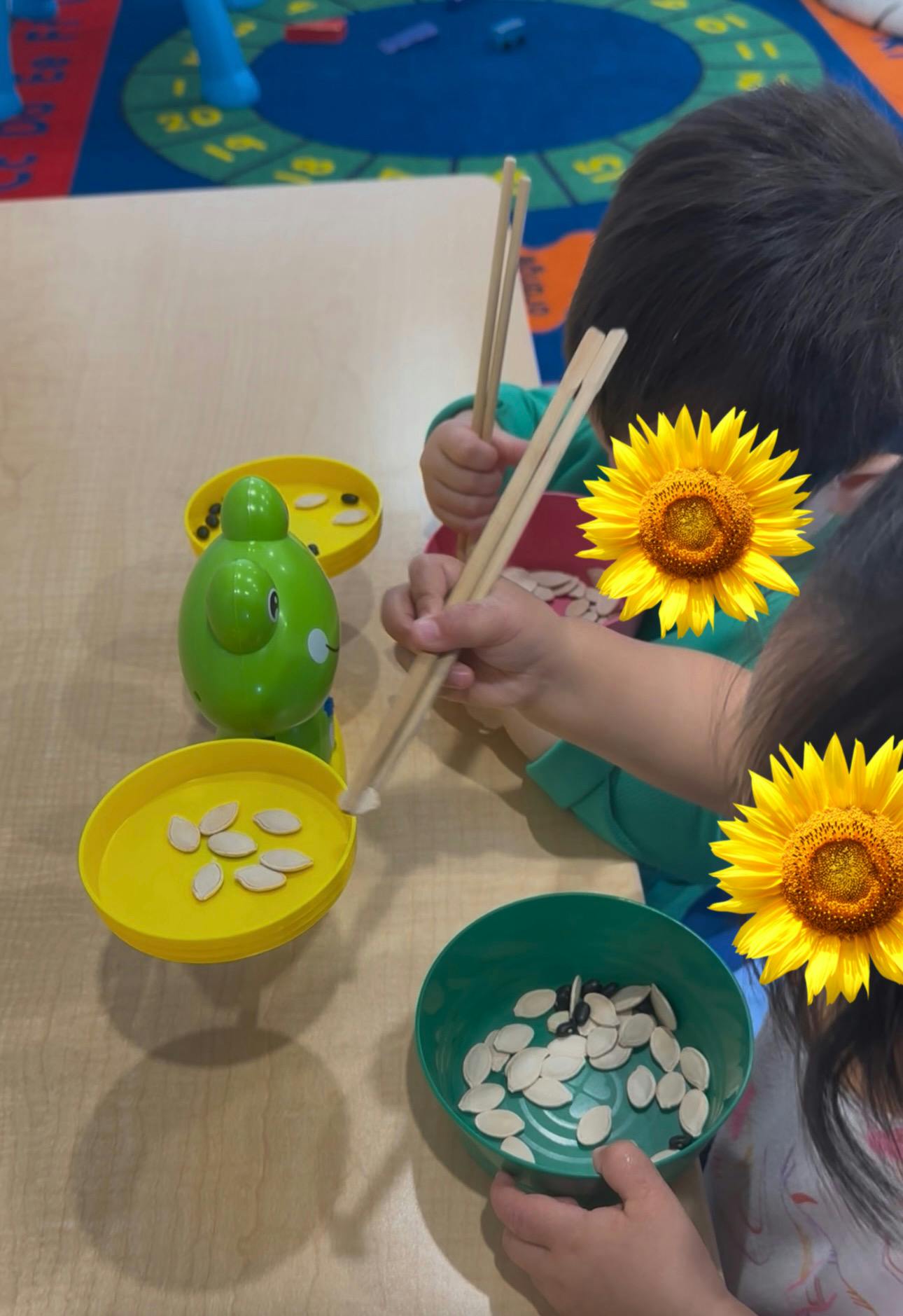 Children using chopsticks to place pumpkin seeds on a green scale toy