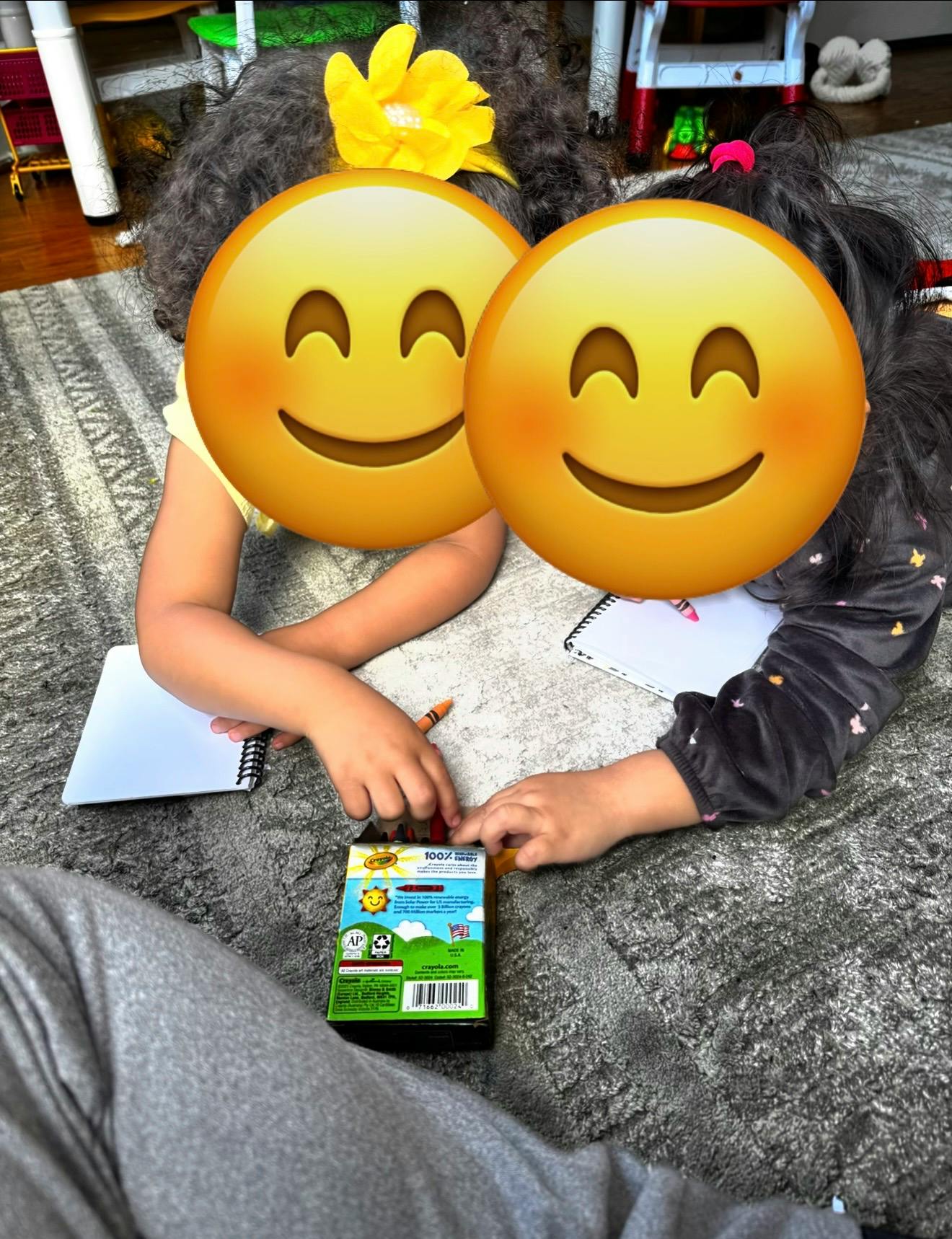Two children drawing with crayons and notebooks on a rug