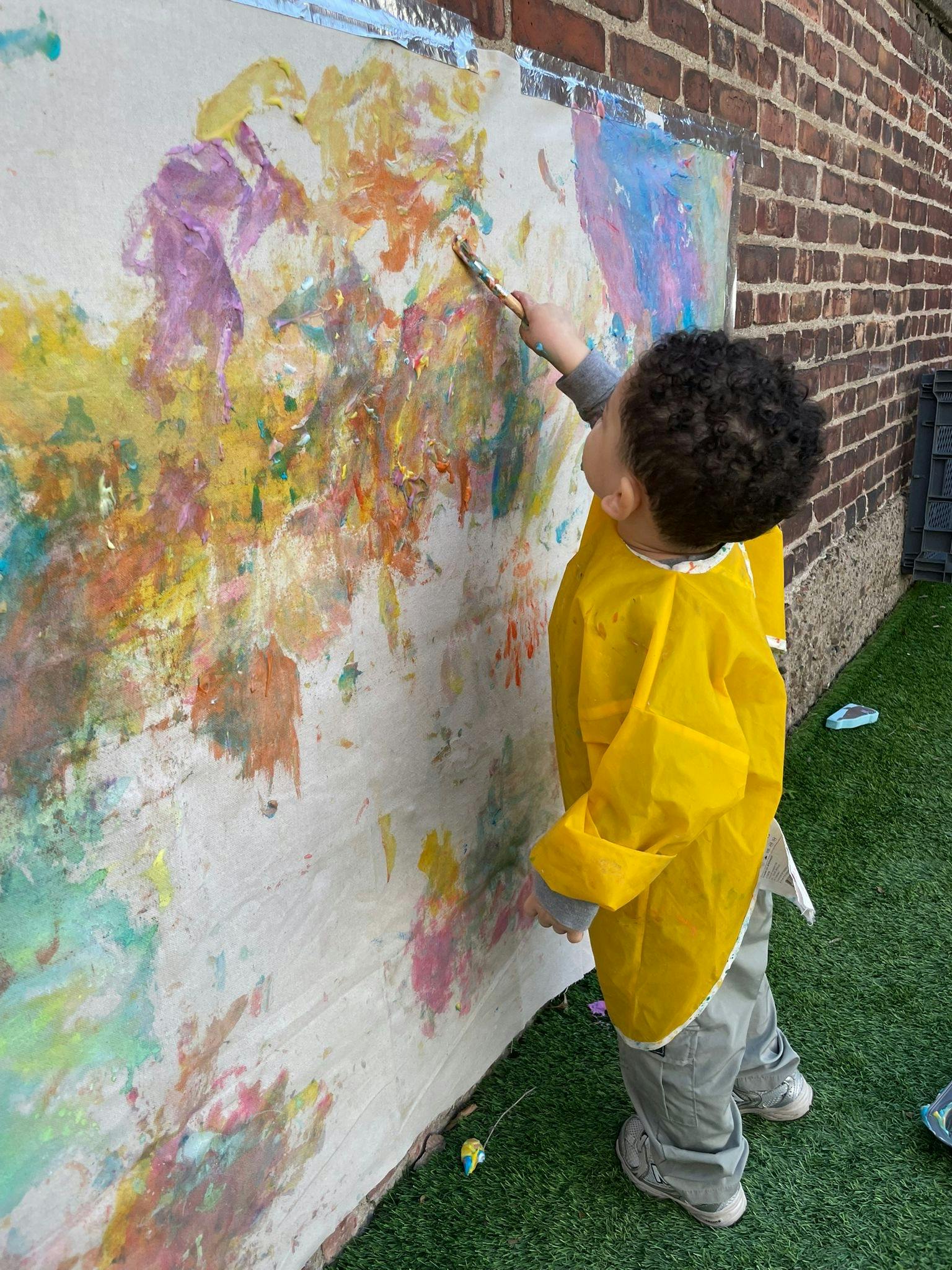 Child in a yellow smock painting on a large canvas