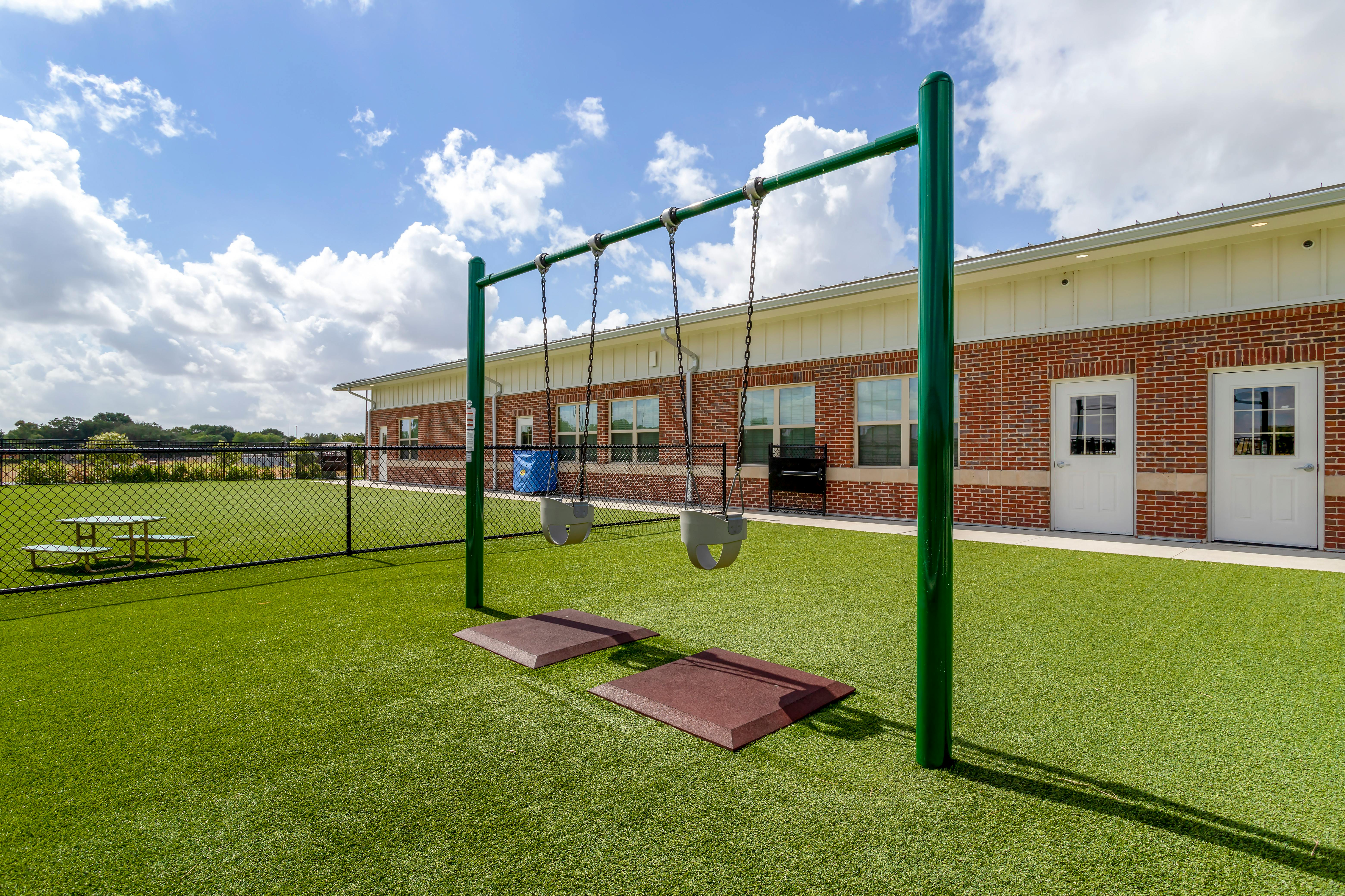 Empty swing set on green turf playground in front of a brick building
