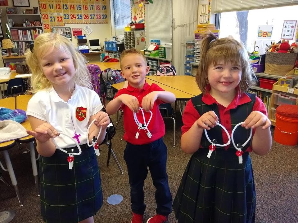 Three children holding up crafts made from pipe cleaners and clothespins in a classroom