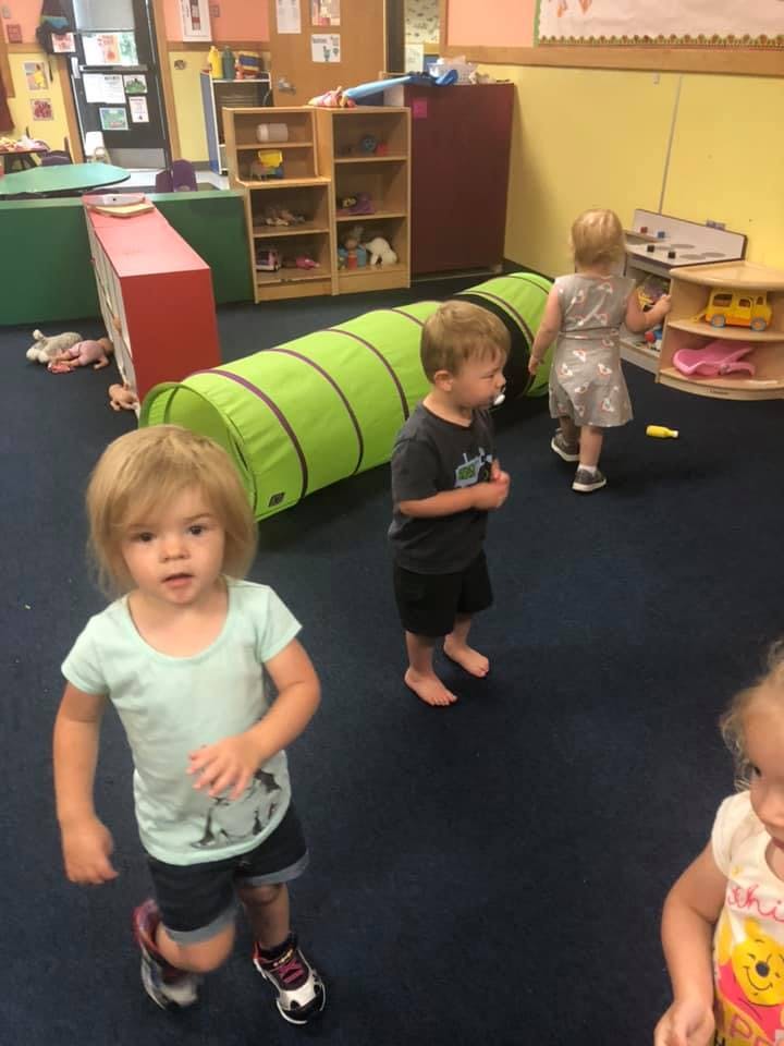 Three children in a classroom with a play tunnel