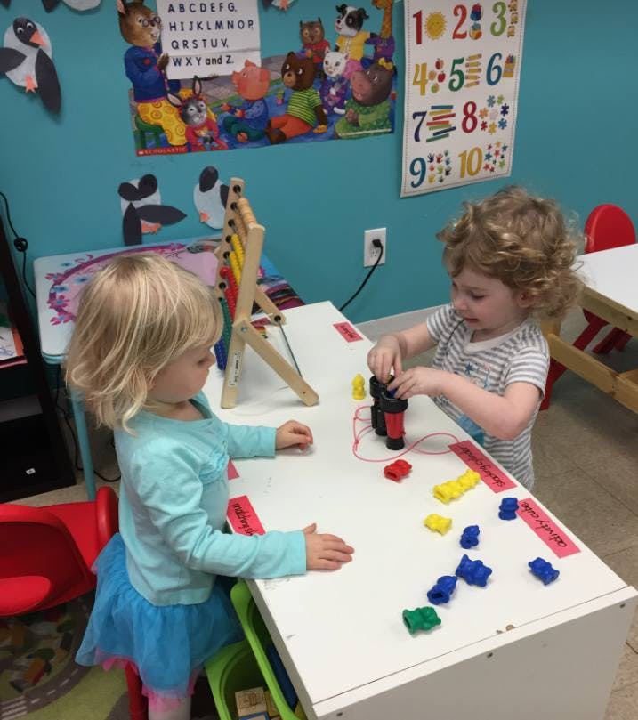 Two children playing with toys at a table in a classroom