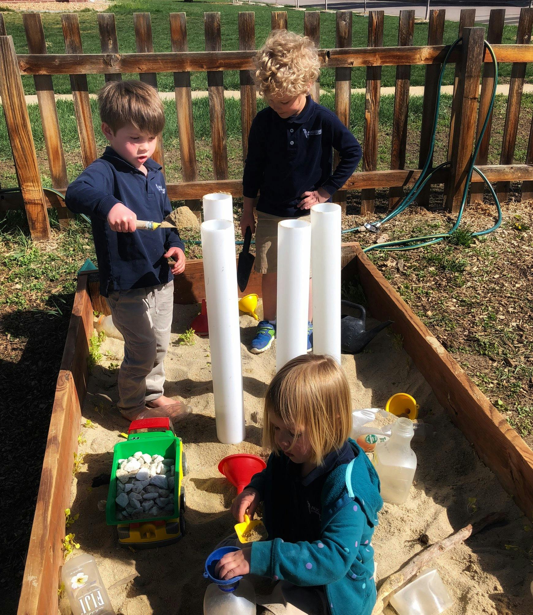 Three children playing in a sandbox with pipes and toys