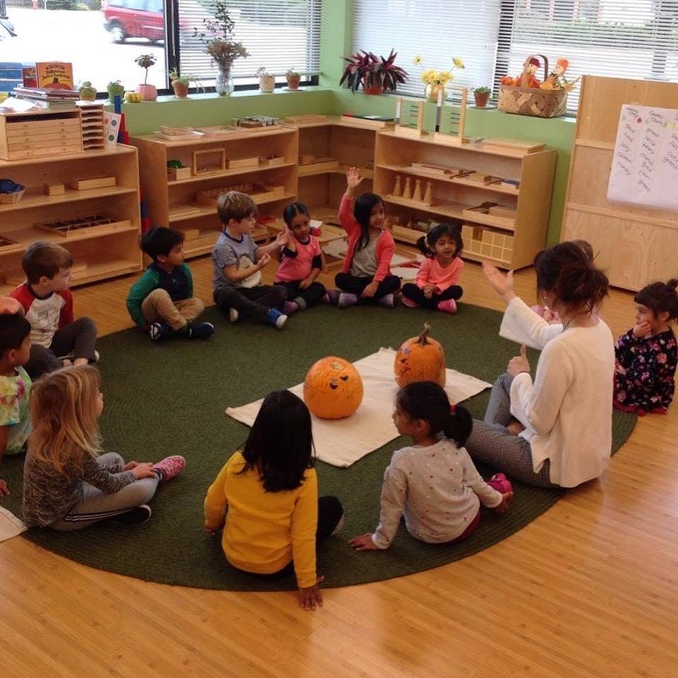 Adult and children sitting in a circle on a rug with pumpkins