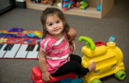 Child sitting on a toy ride-on in a room with a toy piano mat