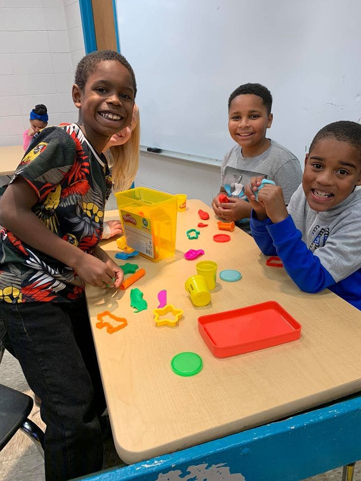 Three children playing with colorful dough and cookie cutters at a table