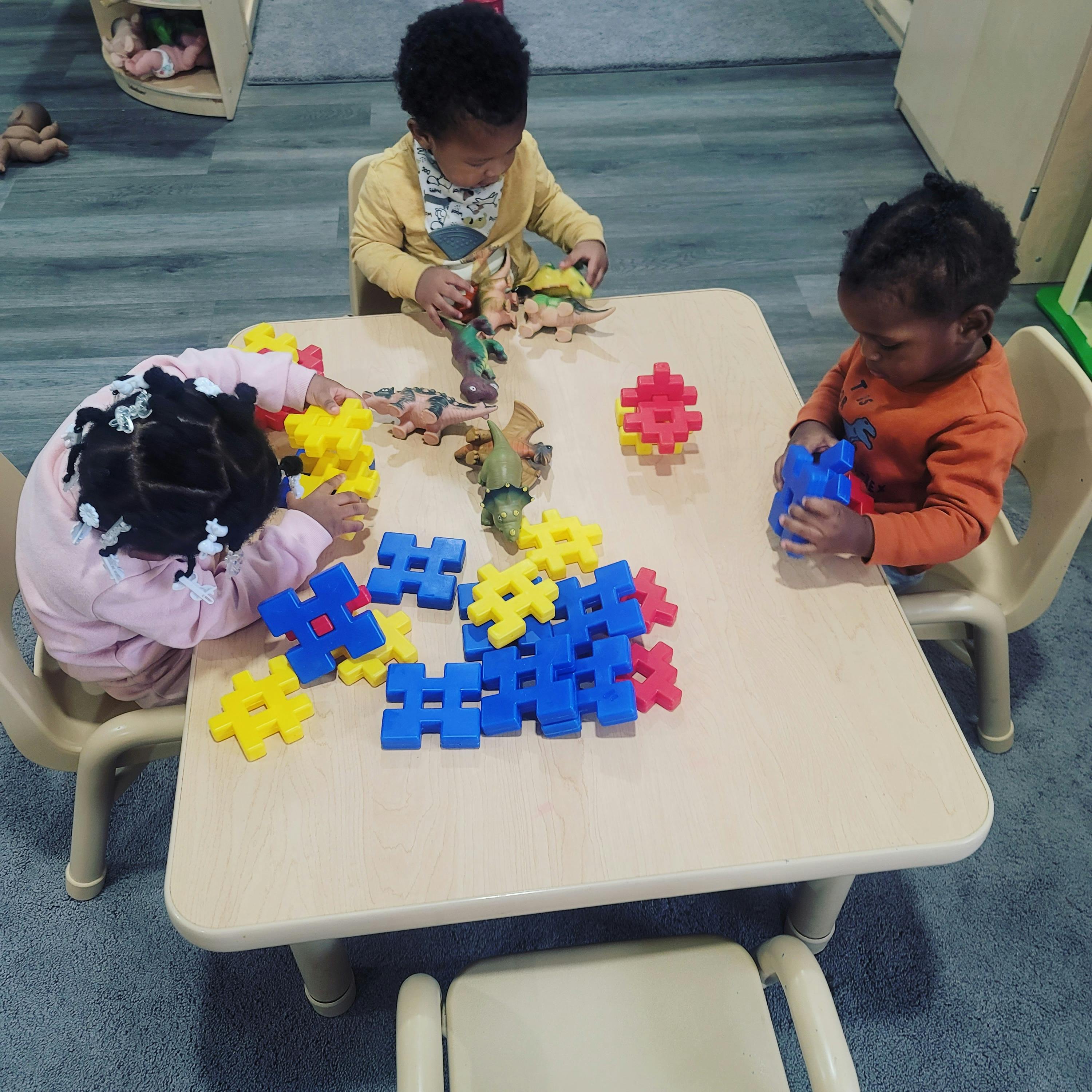 Three children playing with interlocking plastic blocks at a table