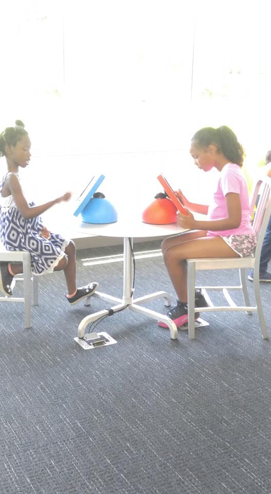 Two children sitting at a table with tablets