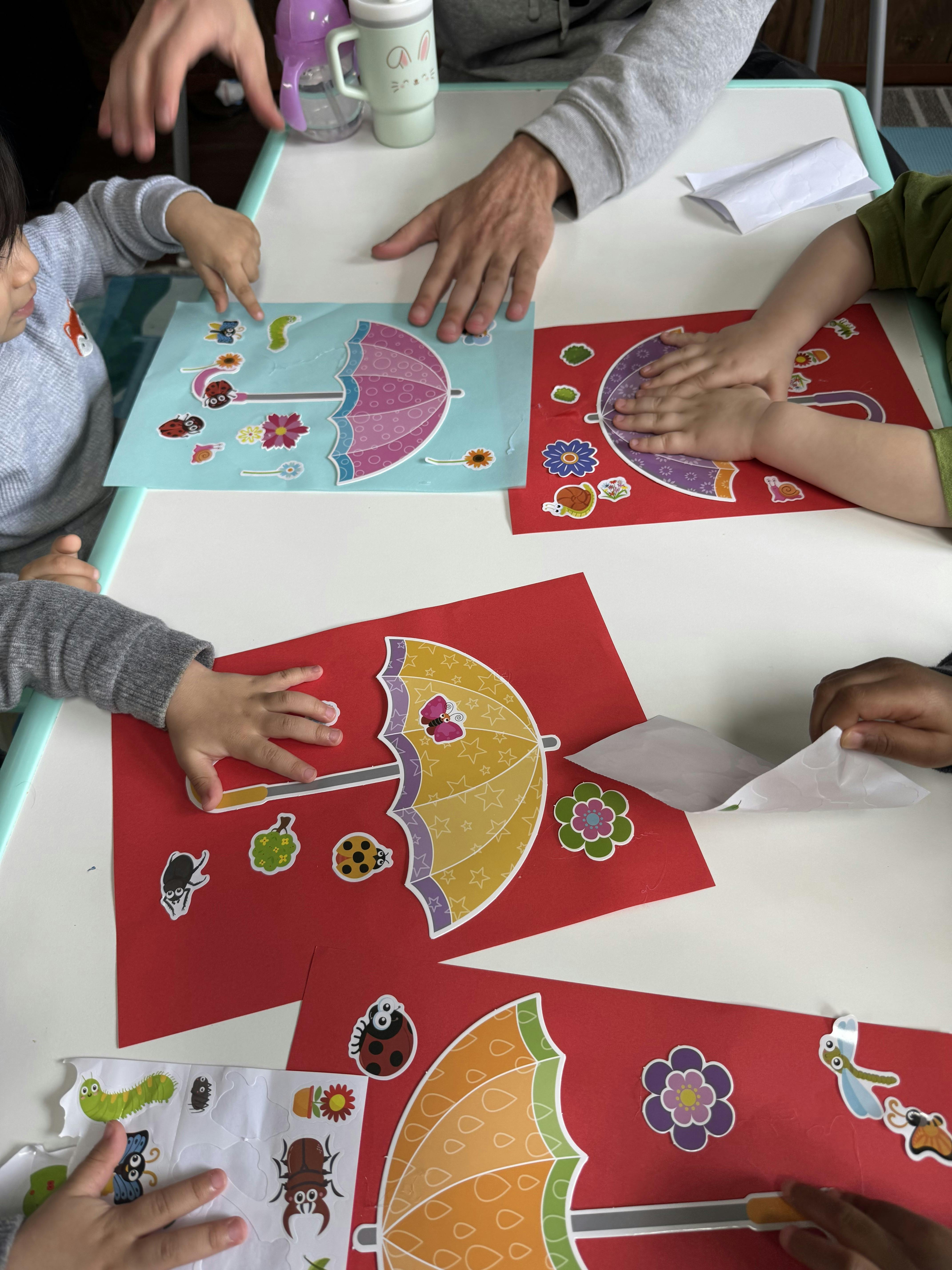 Multiple people doing a craft with stickers of umbrellas, bugs, and flowers