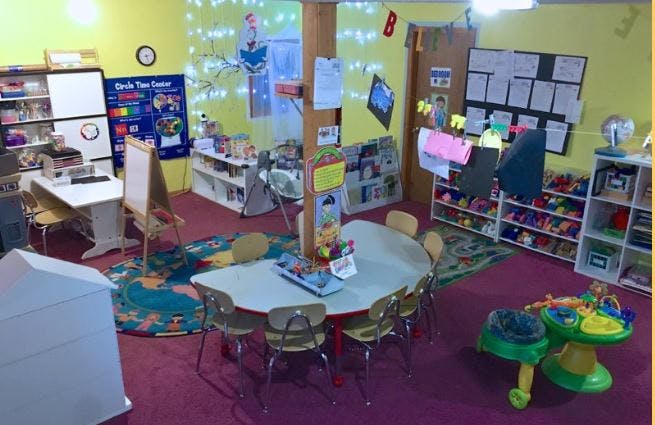 Classroom with small tables and chairs, shelves with toys, and wall decorations