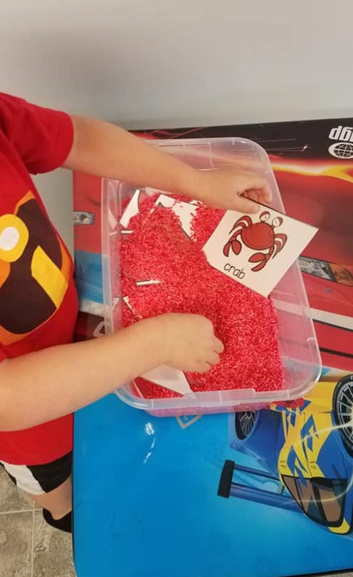 Child playing with red sensory bin filler and a crab flashcard