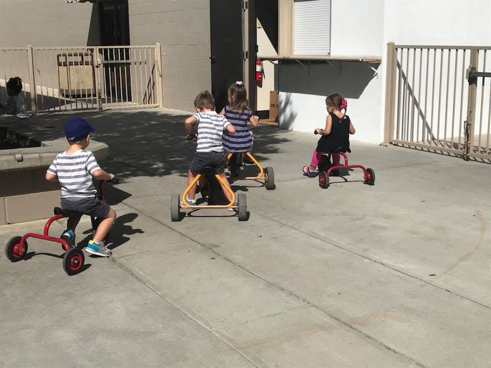 Three children riding tricycles outdoors