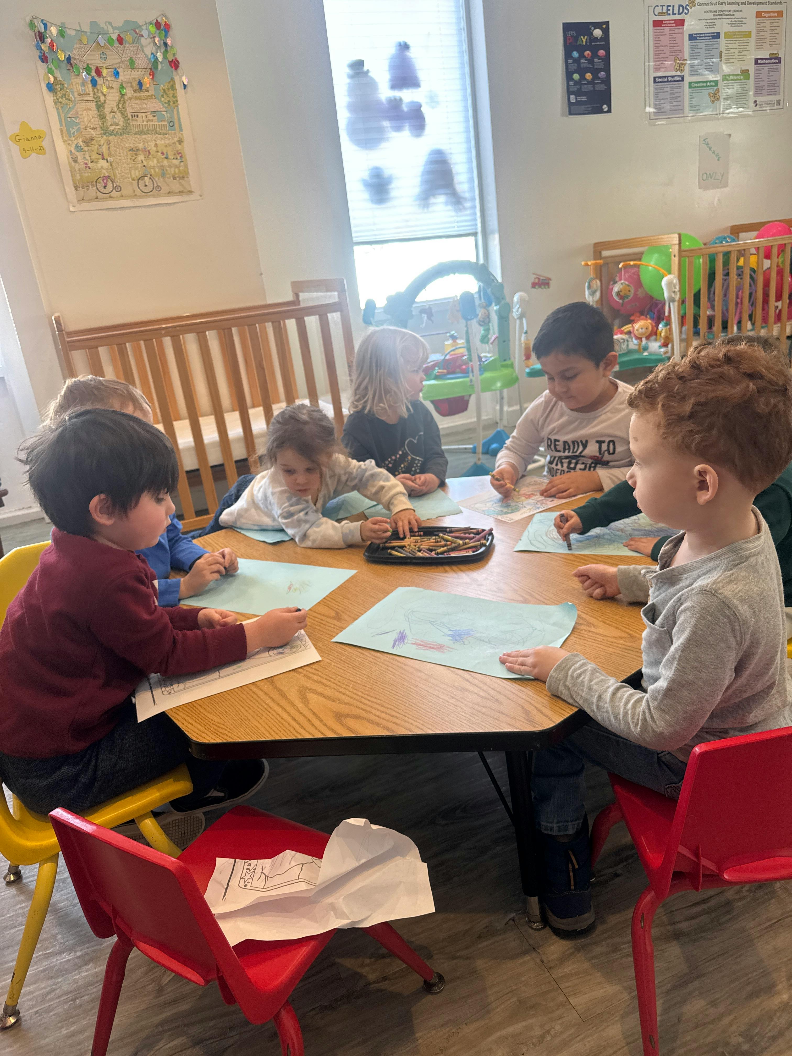 Children sitting at a table coloring with crayons