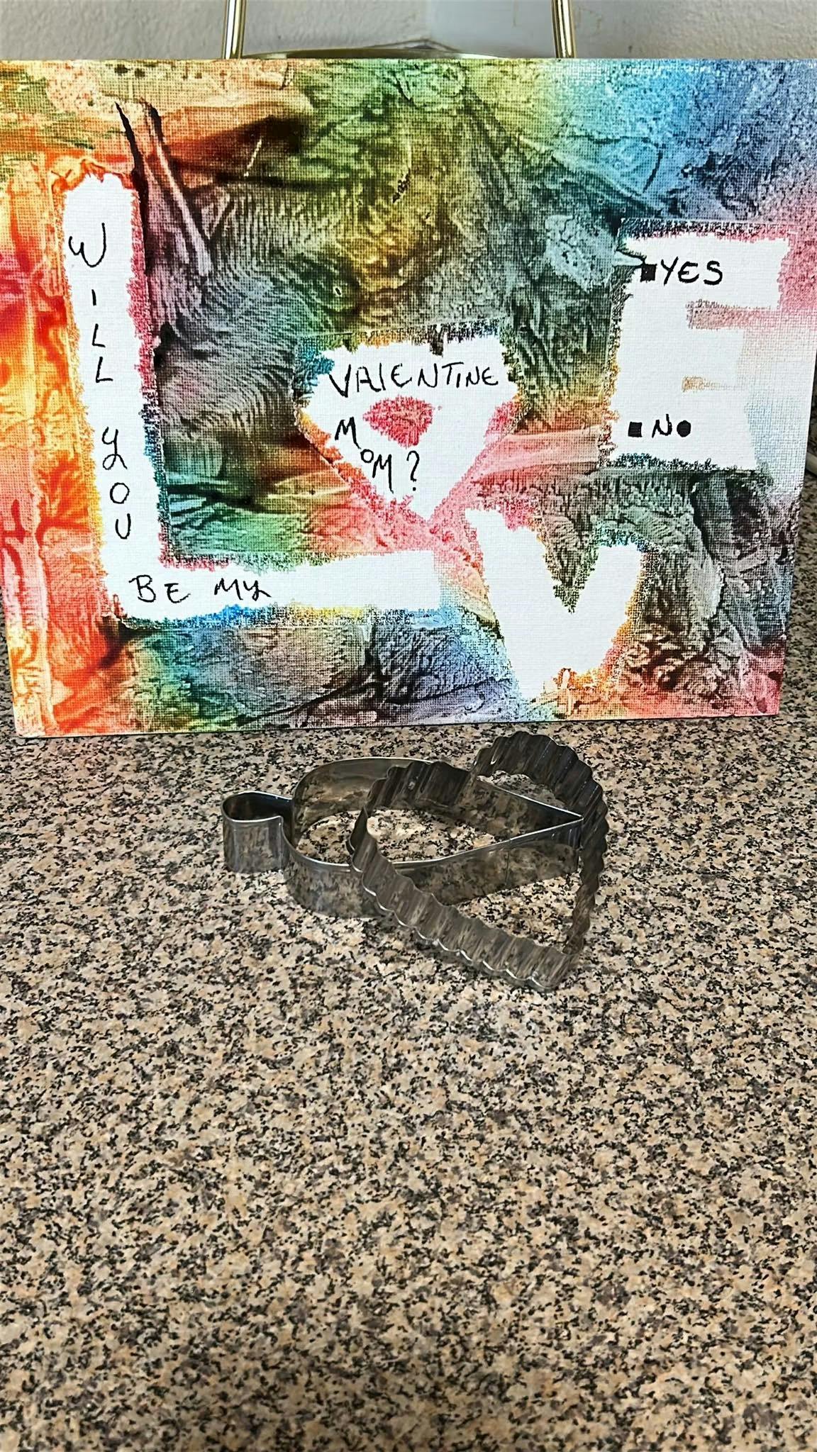 Heart-shaped cookie cutter in front of a painted canvas asking to be a valentine