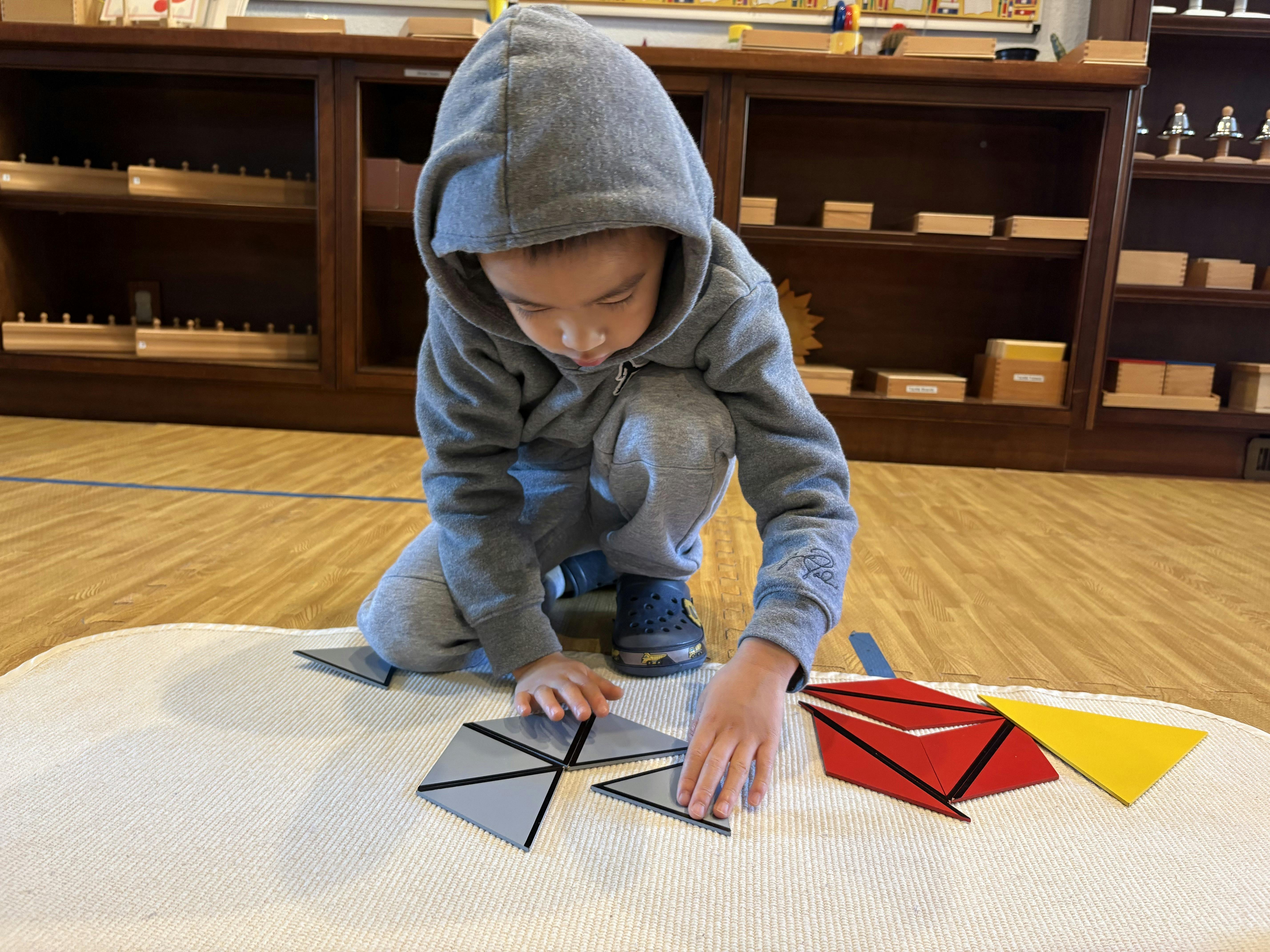 Child crouching on the floor arranging geometric shapes on a mat in a classroom