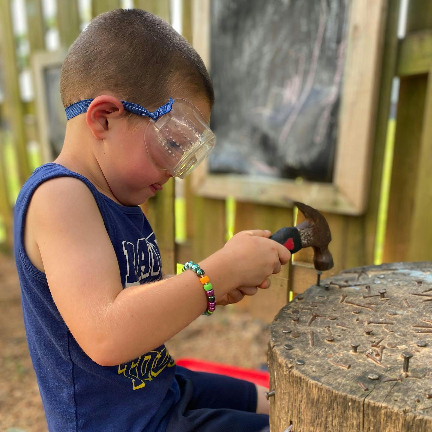 Child wearing safety glasses hammering a nail into a tree stump