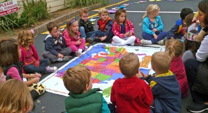Children sitting on the ground around a colorful map
