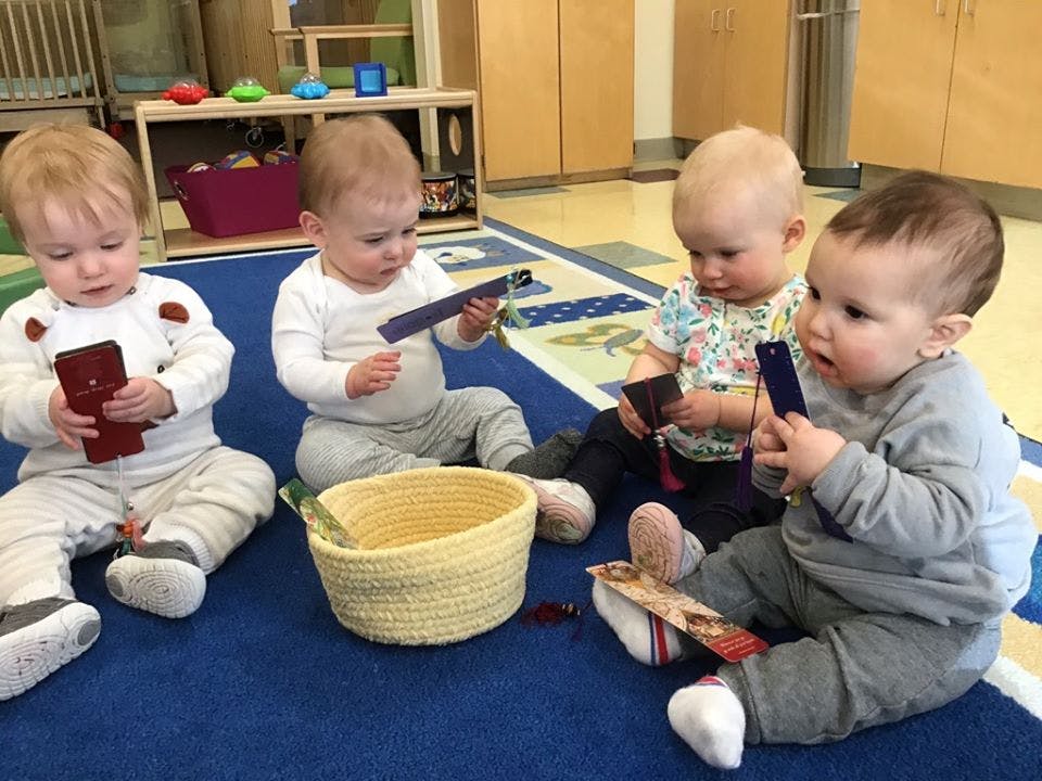 Four babies sitting on a blue rug playing with small objects