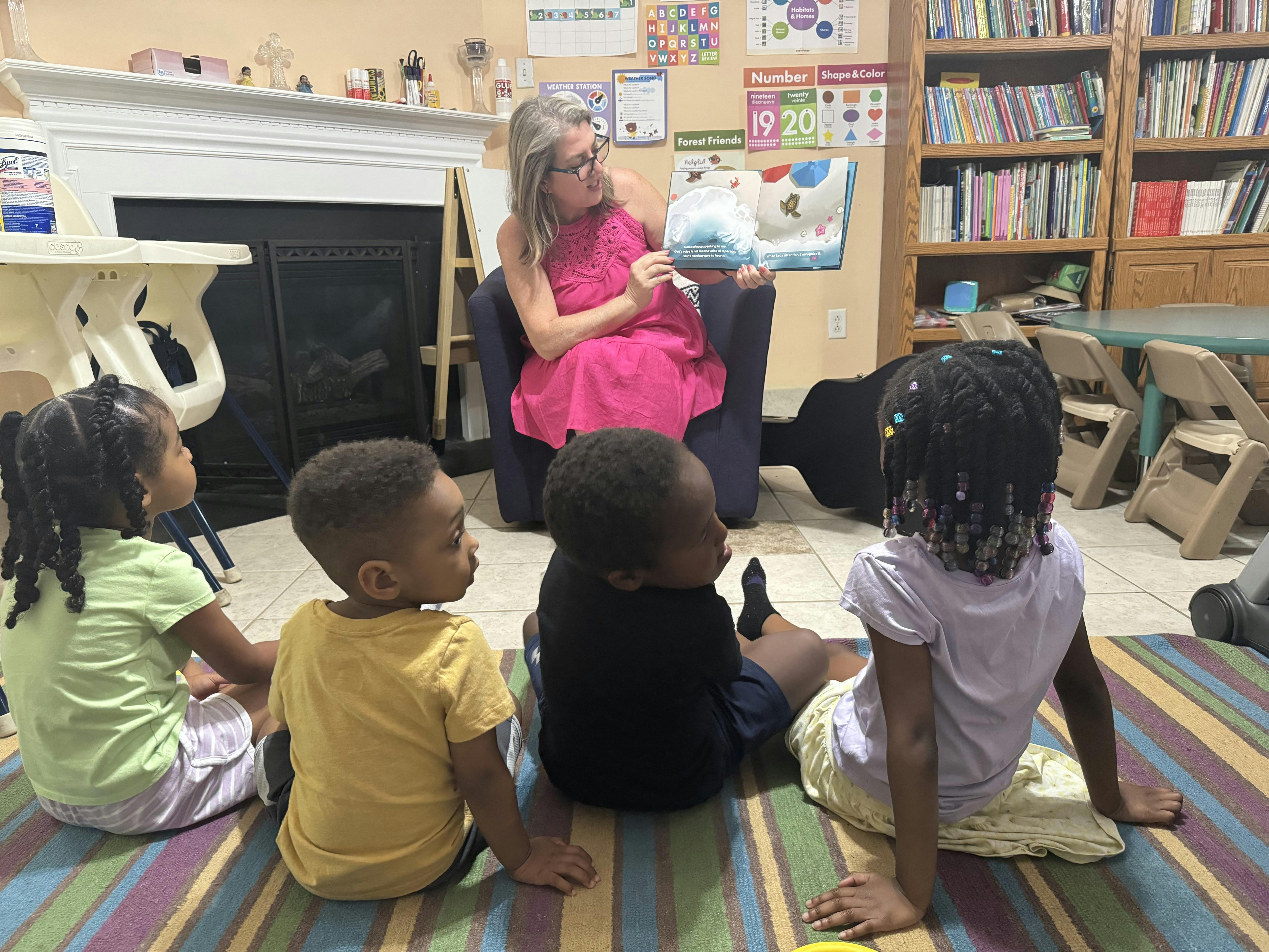 Adult reading a book to four children sitting on a rug in a classroom