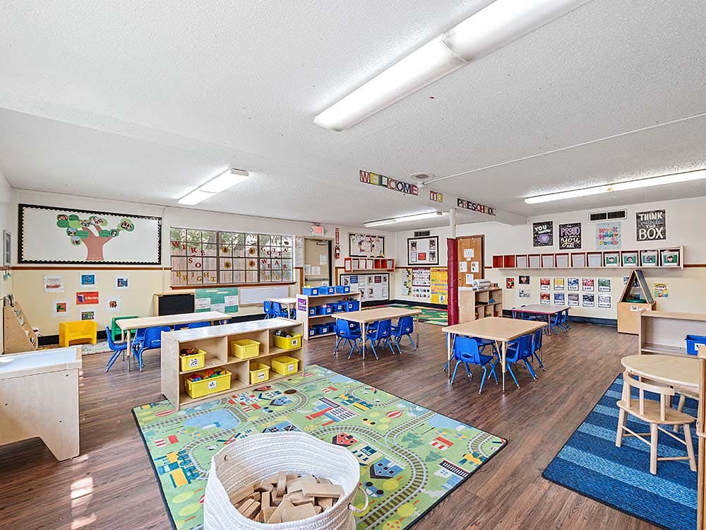 Empty preschool classroom with tables, chairs, and colorful rugs