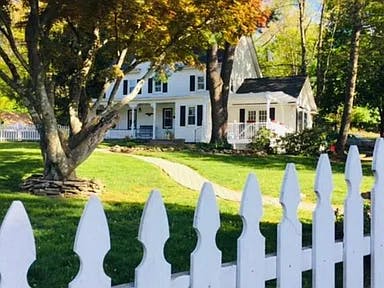 White house with a porch and green lawn behind a white picket fence
